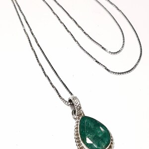 May include: A silver chain necklace with a teardrop-shaped pendant featuring a large green gemstone surrounded by a silver border.