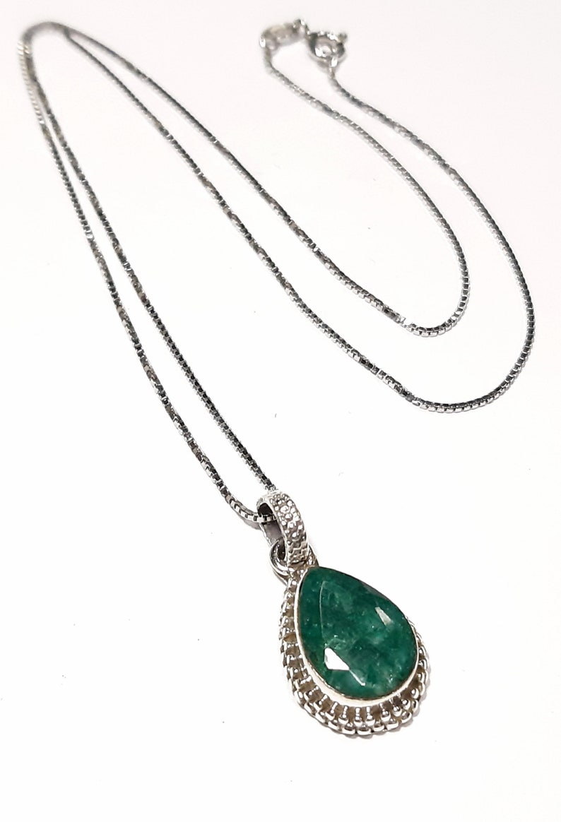 May include: A silver chain necklace with a teardrop-shaped pendant featuring a large green gemstone surrounded by a silver border.