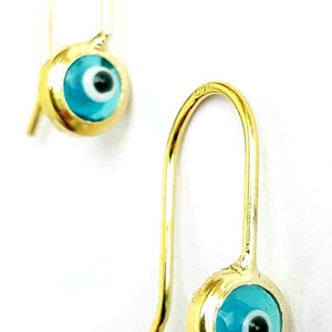 K&ouml;nnte beinhalten: Ein Paar goldene Ohrringe mit blauen b&ouml;sen Augen-Anh&auml;ngern. Die Ohrringe sind aus Gold und haben ein schlichtes Design. Die Anh&auml;nger sind rund und haben eine blaue Emaille-Oberfl&auml;che mit einem wei&szlig;en Auge und einer schwarzen Pupille.
