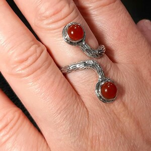 May include: A silver ring with a twisted, branch-like design. The ring has two round, red carnelian gemstones.