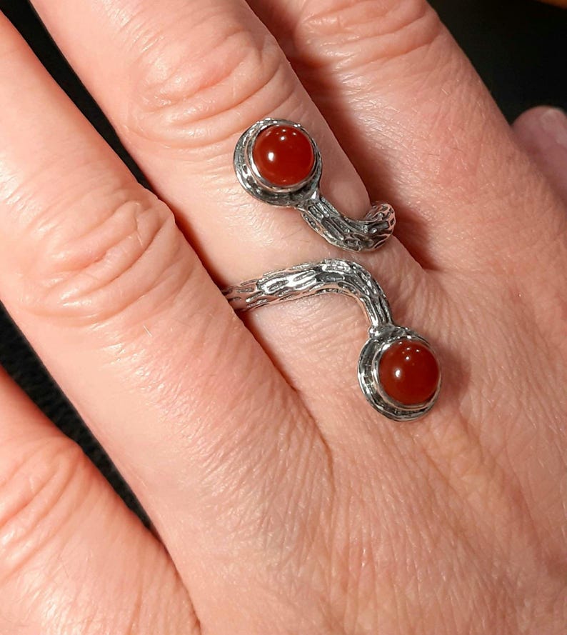 May include: A silver ring with a twisted, branch-like design. The ring has two round, red carnelian gemstones.