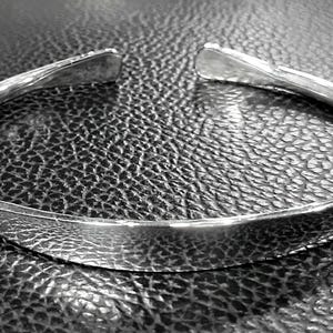 May include: A silver bangle bracelet with a smooth, rounded surface. The bracelet is open and has a simple, minimalist design.