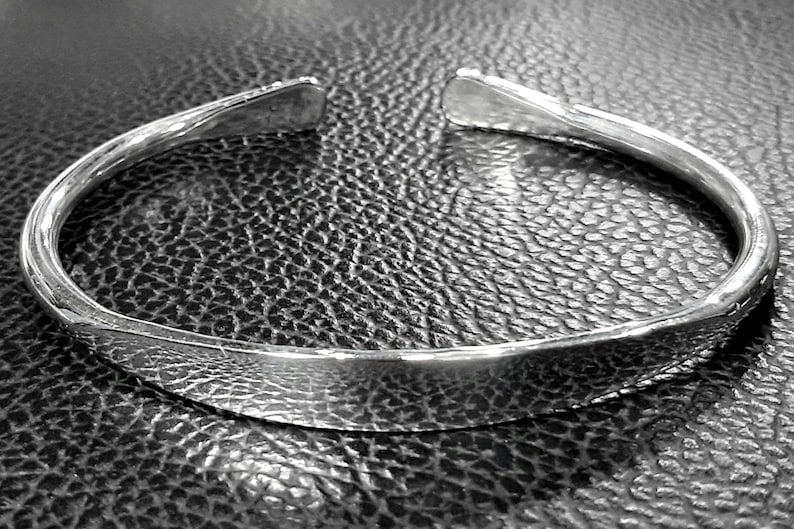 May include: A silver bangle bracelet with a smooth, rounded surface. The bracelet is open and has a simple, minimalist design.