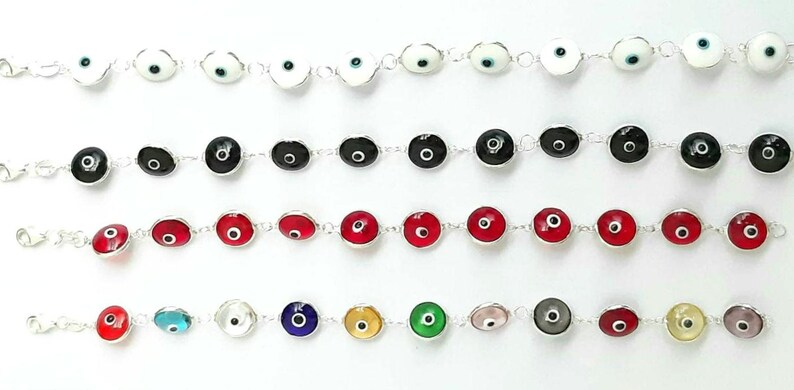 May include: A set of silver bracelets with various colored evil eye charms. The charms are round and have a white, black, red, blue, green, gold, or pink eye in the center.