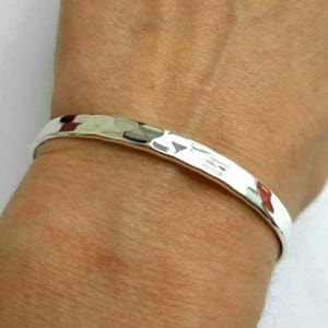 May include: A silver hammered bangle bracelet. The bracelet is smooth and shiny, with a slightly curved shape.