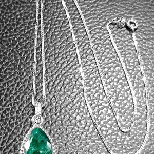 May include: A silver chain necklace with a teardrop-shaped pendant featuring a large, green gemstone.