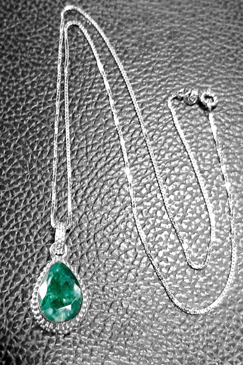 May include: A silver chain necklace with a teardrop-shaped pendant featuring a large, green gemstone.