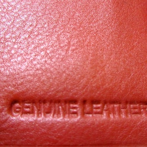 May include: Close-up of a red leather surface with the words "GENUINE LEATHER" embossed in the material.