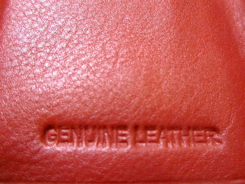 May include: Close-up of a red leather surface with the words "GENUINE LEATHER" embossed in the material.