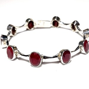 May include: A silver bracelet with red gemstones. The bracelet has a wavy design and is made of sterling silver.
