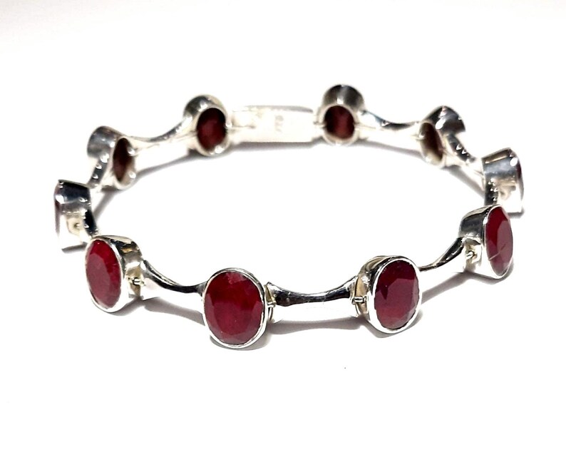 May include: A silver bracelet with red gemstones. The bracelet has a wavy design and is made of sterling silver.