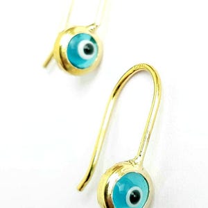 K&ouml;nnte beinhalten: Ein Paar goldene Ohrringe mit blauen b&ouml;sen Augen-Anh&auml;ngern. Die Ohrringe haben ein schlichtes Haken-Design.