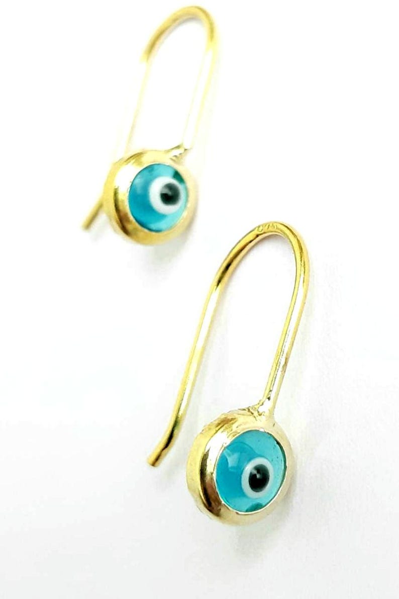 K&ouml;nnte beinhalten: Ein Paar goldene Ohrringe mit blauen b&ouml;sen Augen-Anh&auml;ngern. Die Ohrringe haben ein schlichtes Haken-Design.