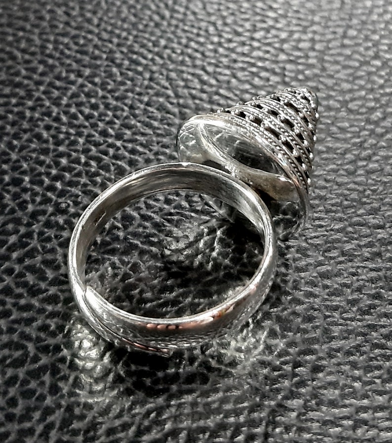 May include: A silver ring with a cone-shaped top. The cone is decorated with a geometric pattern.