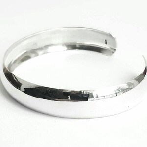 May include: A silver bangle bracelet with a smooth, rounded surface.