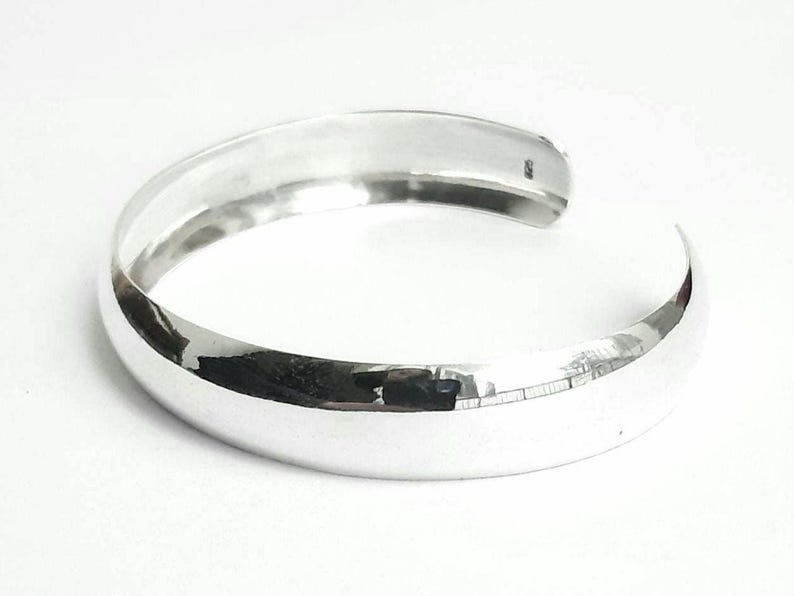 May include: A silver bangle bracelet with a smooth, rounded surface.