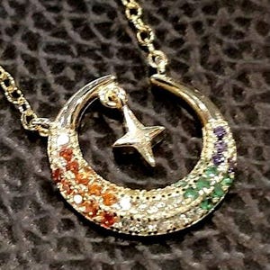 May include: A gold crescent moon necklace with a star charm. The crescent moon is adorned with a rainbow of colorful gemstones.
