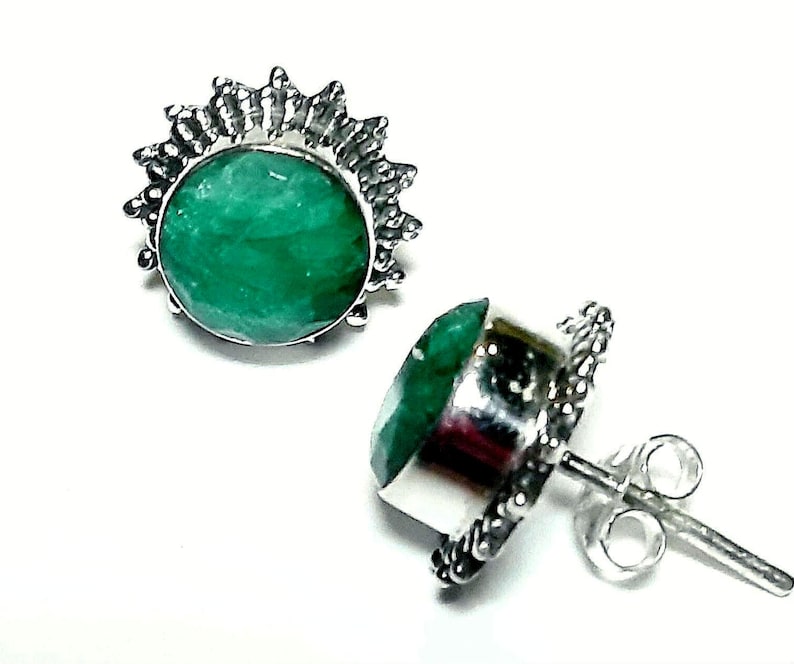 Puede incluir: Un par de pendientes de bot&oacute;n con una vibrante piedra preciosa verde engastada en un marco plateado con forma de sol. Los pendientes tienen cierre de poste y mariposa, mostrando un dise&ntilde;o cl&aacute;sico.