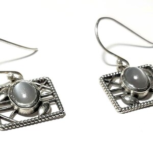 May include: A pair of silver earrings with a white oval gemstone set in a geometric design.