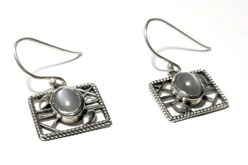 May include: A pair of silver earrings with a white oval gemstone set in a geometric design.