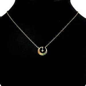 May include: A gold chain necklace with a crescent moon pendant. The moon is decorated with colorful gemstones and a small star.