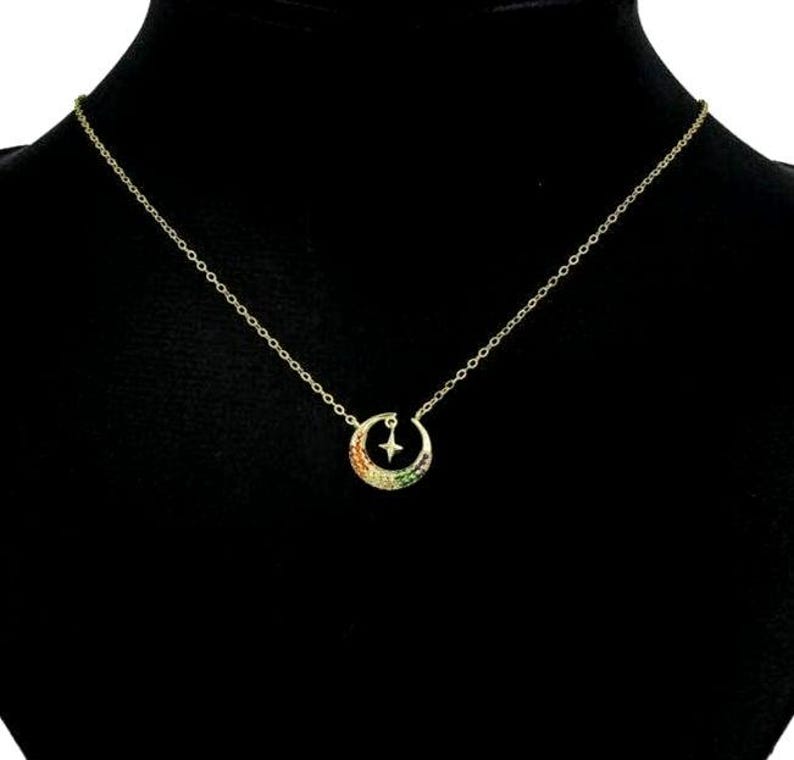 May include: A gold chain necklace with a crescent moon pendant. The moon is decorated with colorful gemstones and a small star.