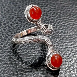 May include: A silver ring with a twisted, branch-like design. The ring features two red carnelian gemstones.