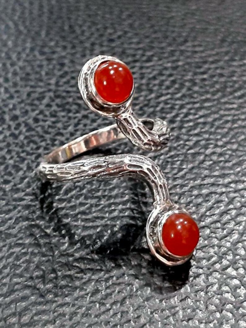 May include: A silver ring with a twisted, branch-like design. The ring features two red carnelian gemstones.