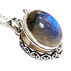 Peut inclure: Un collier avec un pendentif en argent en forme de m&eacute;daillon orn&eacute; d'une pierre de labradorite bleue et grise. Le m&eacute;daillon est ouvert et pr&eacute;sente un motif d&eacute;licat et orn&eacute;.