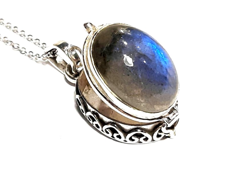 Peut inclure: Un collier avec un pendentif en argent en forme de m&eacute;daillon orn&eacute; d'une pierre de labradorite bleue et grise. Le m&eacute;daillon est ouvert et pr&eacute;sente un motif d&eacute;licat et orn&eacute;.