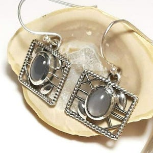 May include: A pair of silver earrings with a gray stone set in a geometric design.