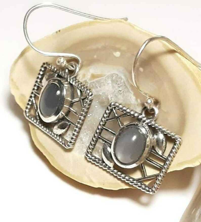 May include: A pair of silver earrings with a gray stone set in a geometric design.