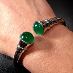Peut inclure: Un bracelet jonc en argent avec deux cabochons de pierres précieuses vertes. Le bracelet est ouvert et possède une fermeture à charnière.