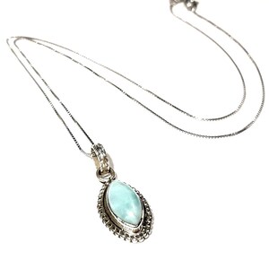 May include: A silver chain necklace with a light blue gemstone pendant. The pendant is oval shaped and has a silver filigree design around the edge.