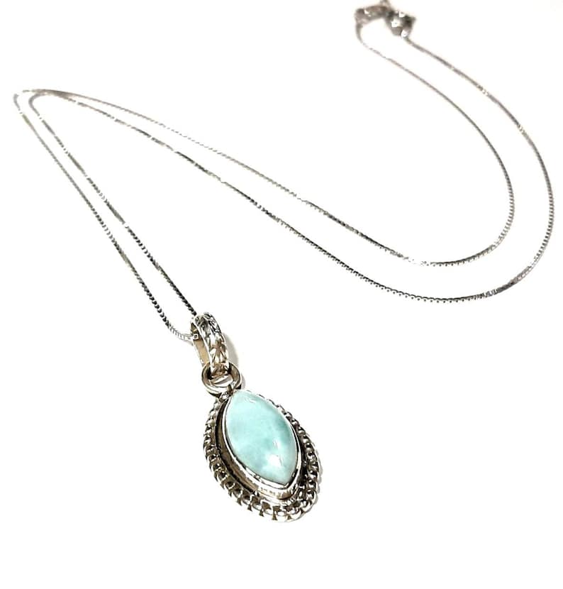 May include: A silver chain necklace with a light blue gemstone pendant. The pendant is oval shaped and has a silver filigree design around the edge.
