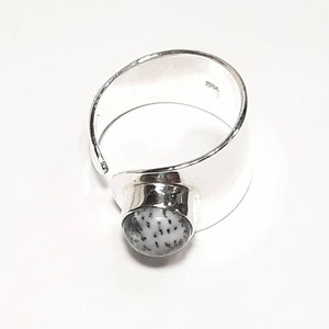 May include: A silver ring with a white and gray stone set in the center. The ring is open on one side and has a wide band.