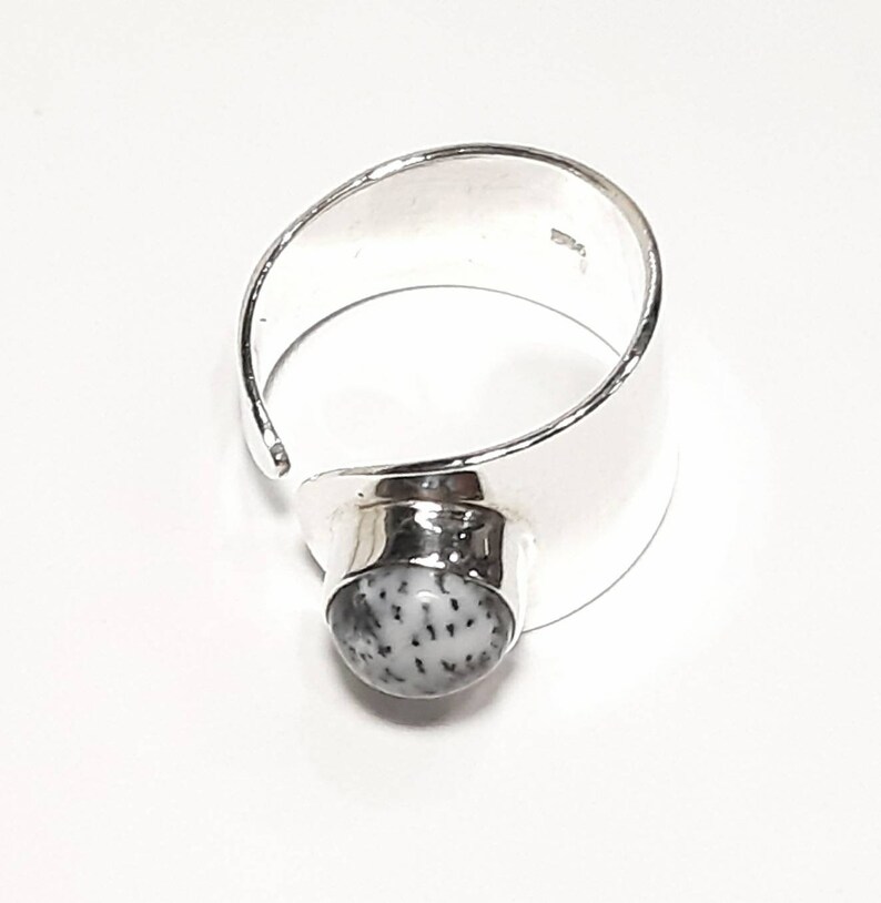 May include: A silver ring with a white and gray stone set in the center. The ring is open on one side and has a wide band.
