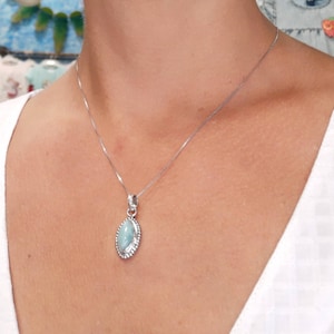 May include: A silver chain necklace with a light blue oval pendant. The pendant has a silver border.