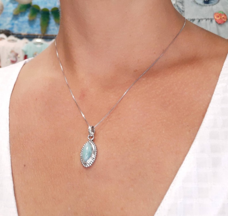 May include: A silver chain necklace with a light blue oval pendant. The pendant has a silver border.