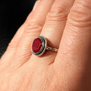 Pu&ograve; includere: Un anello d'argento con una pietra preziosa rossa incastonata in una lunetta circolare. L'anello ha una fascia attorcigliata.