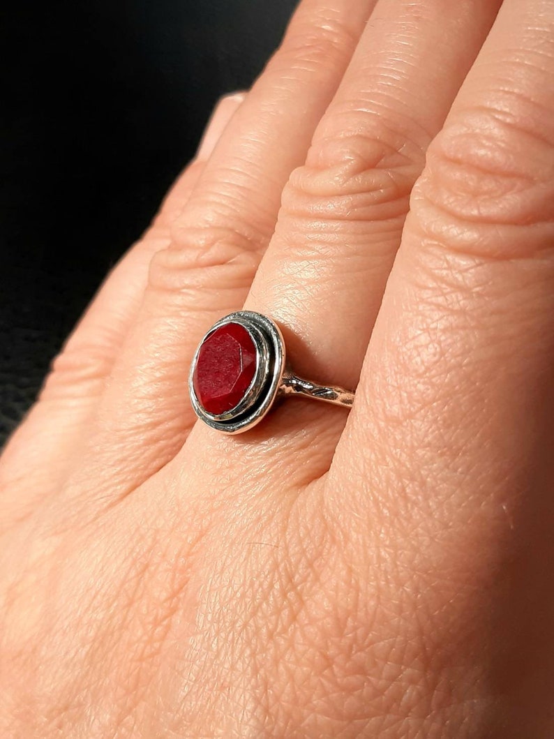 Pu&ograve; includere: Un anello d'argento con una pietra preziosa rossa incastonata in una lunetta circolare. L'anello ha una fascia attorcigliata.