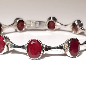 May include: A silver bracelet with red oval-shaped gemstones. The bracelet has a simple design with a repeating pattern of gemstones and silver bars.