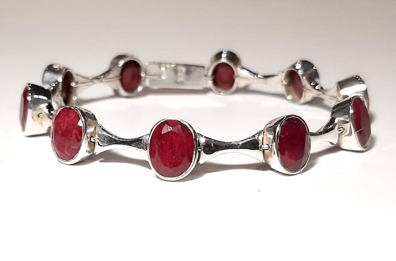 May include: A silver bracelet with red oval-shaped gemstones. The bracelet has a simple design with a repeating pattern of gemstones and silver bars.