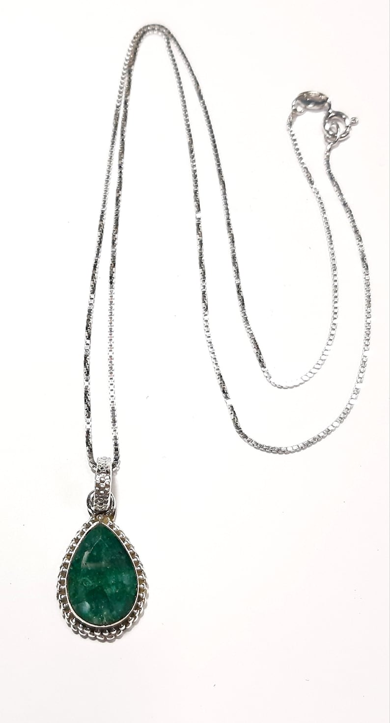 May include: A silver chain necklace with a teardrop-shaped pendant featuring a green gemstone.