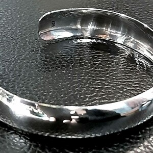 May include: A silver bangle bracelet with a smooth, rounded surface. The bracelet has a hallmark of "925" on the inside.