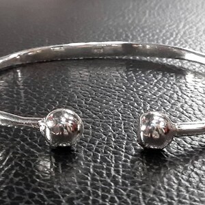 Op de afbeelding: Een zilveren armband met twee ronde, getextureerde ballen aan de uiteinden.