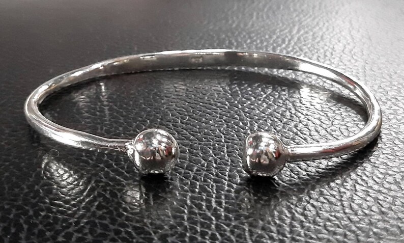 Op de afbeelding: Een zilveren armband met twee ronde, getextureerde ballen aan de uiteinden.