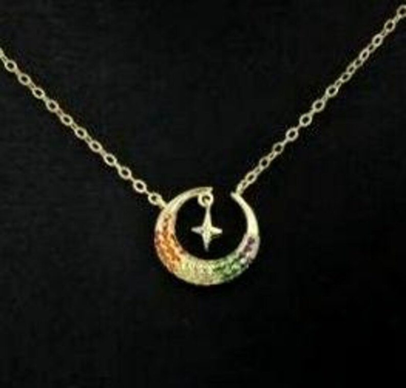 May include: A gold crescent moon necklace with a small star charm. The moon is decorated with colorful cubic zirconia stones.