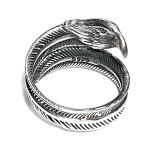 May include: A silver-colored ring with a detailed eagle head design. The ring wraps around the finger with a feather motif. The ring is marked with "S925".