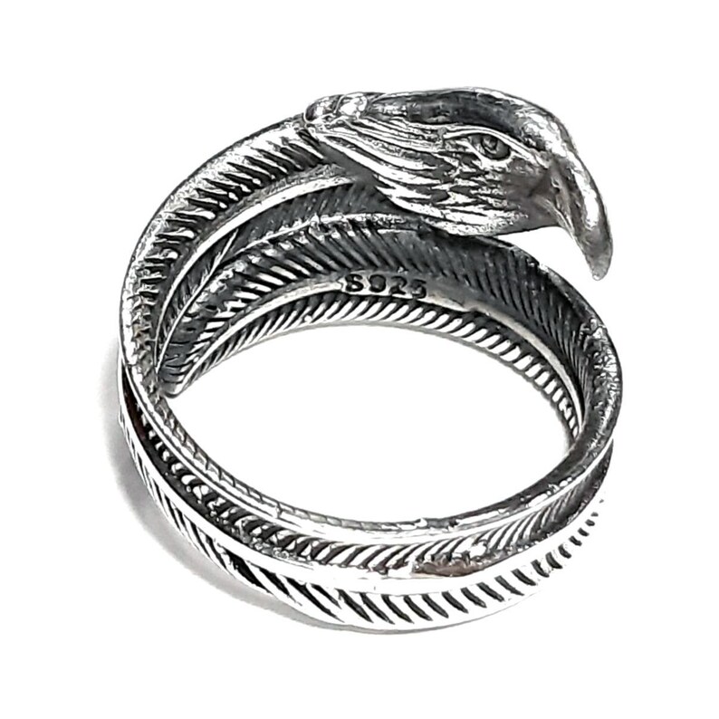 May include: A silver-colored ring with a detailed eagle head design. The ring wraps around the finger with a feather motif. The ring is marked with "S925".